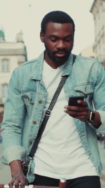 Canlı bir şehir ortamında akıllı telefonuyla meşgul olan bir adam gelişigüzel giyinmiş ve öylesine geziniyor.