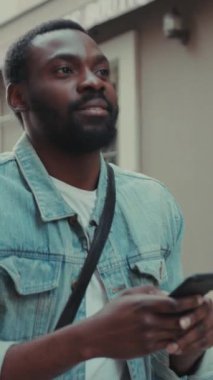 Çevresi canlı bir şehir manzarasıyla çevriliyken akıllı telefonuyla mesajları okumaya odaklanmış genç bir adam.