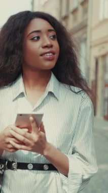 Şık bir genç kadın akıllı telefonuna dalmış, bir şehir caddesinde dijital etkileşimlere dalmış.