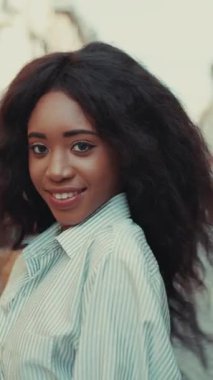 Kıvırcık saçlı bir kadın, hareketli bir şehir ortamında arkadan görülüyor, özgün anları yakalıyor.