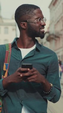 Gülümseyen genç bir adam akıllı telefonuyla iletişim kurar, modern şehir yaşam tarzını ve bağlantılarını gösterir..