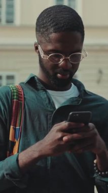 Şık ve şık giyinmiş genç bir adam akıllı telefonuyla meşgul oluyor ve modern şehir yaşam tarzını sergiliyor.