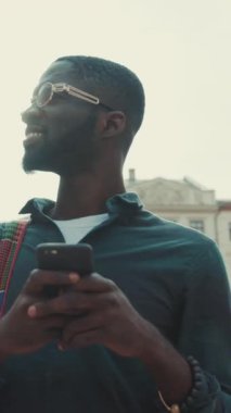 Şık ve şık bir genç adam, parlak bir şehir manzarasının tadını çıkarırken telefonunu rastgele kontrol ediyor.