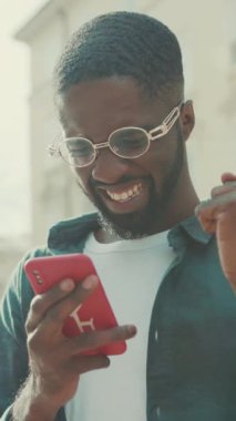 Neşeli bir adam, şehrin canlılığı arasında modern bağlantıyı gösteren akıllı telefonuyla meşgul olur.