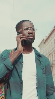 Genç bir adam şık ve canlı bir şehir çevresi ile çevriliyken akıllı telefonuyla meşgul olarak görülüyor.