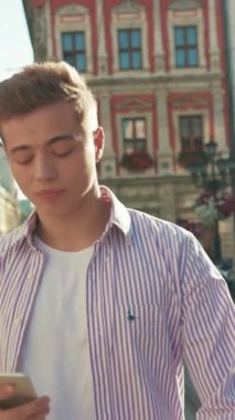 Portre genç mutlu adam sokakta yürür etrafına bak gülümse güneş ışığı sevimli iş mobil aygıtı şehir dışında akıllı telefon teknolojisi yakışıklı dokunmatik ekranı yavaş çekim kapat