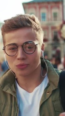 Gözlüklü genç adam sokakta dans ediyor kulaklıkla müzik dinliyor cep telefonuyla gülümsüyor cep telefonuyla geziyor mobil aletler açık havada akıllı telefon teknolojisi yakışıklı hippi yavaş çekimde portreyi kapat