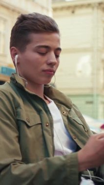 Çekici genç adam telefon kullanıyor. Kulaklıkla müzik dinliyor. Gülümsüyor, gülümsüyor.