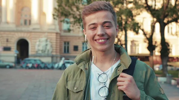 Kulaklıklı genç adam, kameraya bak. Gülümse. Sokakta mutlu ol. Güneş ışığı.