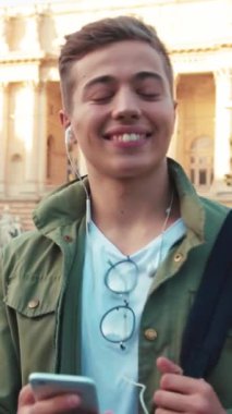 Genç, mutlu, yakışıklı bir genç telefon kullanıyor. Kulaklıkla müzik dinliyor. Etrafına bir bak.