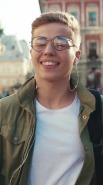 Yavaş çekim, gözlüklü genç adam sokakta dans ediyor kulaklıkla müzik dinliyor, cep telefonuyla gülümsüyor, cep telefonuyla geziyor açık havada geziyor akıllı telefon teknolojisi yakışıklı hippi portreyi kapatıyor.