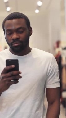 Genç bir adam şık bir mağazada alışveriş yaparken akıllı telefonuyla meşgul oluyor ve modern tüketici davranışları sergiliyor..