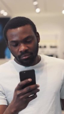 Aktif bir perakende satış ortamında akıllı telefonuna yoğun bir şekilde bakan kendini adamış ve odaklanmış bir adam.