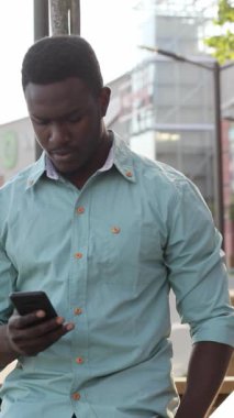 Genç bir adam şehir çevresi ile çevrili akıllı telefonuna odaklanıyor, modern yaşam tarzını sergiliyor..