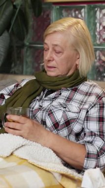 Battaniyenin altında, elinde akıllı telefonla kanepede yatan mutsuz, hasta bir kadın. Oturma odasında aletlerle yalnız büyükannenin portresi. Hastalık. Kapalı.