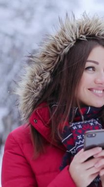 Kırmızı ceketli bir kadın, cep telefonuyla karlı bir arazide geziniyor. Kar taneleri, sarı bir arabanın ortaya çıkmasıyla dayanıklılık gösteren bir zemin oluşturur.