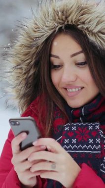 Bu kış sahnesinde, kırmızı ceketli bir kadın ve kürklü ceketli başka bir kadın telefonlarıyla karlı bir zemin oluşturuyorlar, teknolojiyi doğayla harmanlıyorlar.