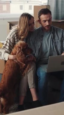 Bir erkek ve bir kadın, köpekleriyle koltukta rahat bir şekilde dizüstü bilgisayara bakıp gülüşlerini ve kahkahalarını paylaşırken sıcak bir anın tadını çıkarırlar.