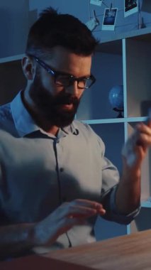 Bu videoda, gözlüklü sakallı bir adam iş ortamında birden fazla iş yapıyor, tablet kullanıyor ve sorunsuz bir şekilde telefon görüşmelerine geçiyor.