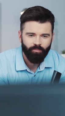 Bu videoda, sakallı bir adam dijital dünyasında geziniyor, bilgisayarı, laptopu ve cep telefonu arasında birden fazla iş yapıyor, modern yaşam tarzını gösteriyor.