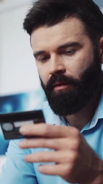 Tanınmış, bakımlı bir sakalı olan bir adam şu anda faaliyetlerini sürdürürken elinde sıkıca bir kredi kartı tutuyor.