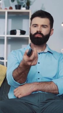 Mavi gömlekli, sakallı, rahat bir adam koltukta, uzaktan kumandayla ve telefonla vakit geçirmekten zevk alır. Sonra da kendine güvenen bir mikrofon tutar.