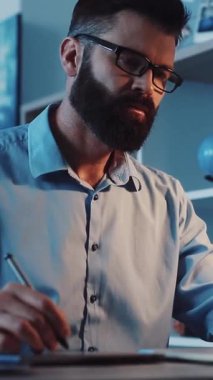 Videoda sakallı ve gözlüklü düşünceli bir adam var, sakin bir arkaplanda yazıya dalmış, özverisini sergiliyor