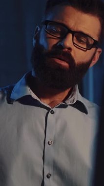 Gözlüklü sakallı bir adam mavi gömlekli işine odaklanmış vazifesinin stresinden dolayı terleyen bir tablet ve bilgisayar kullanıyor.