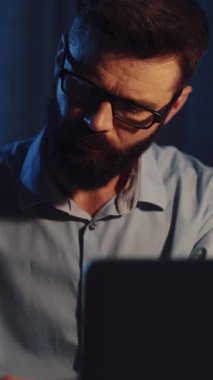 Bu videoda, gözlüklü sakallı bir adam dikkatle dizüstü bilgisayarında çalışıyor, bilgiyi analiz ediyor, daktilo ediyor, konsantrasyon ve verimliliği gösteriyor.