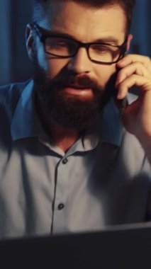 Odaklanmış bir sahnede, gözlüklü, masada oturan, modern iş iletişimi ve profesyonelliği vurgulayan sakallı bir adam görülüyor.