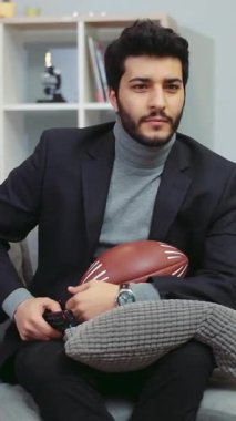 Bu neşeli videoda, takım elbiseli bir adam bir kanepede futbol topu ve uzaktan kumandayla rahatlıyor, eğlence ve spor kültürünün neşesini somutlaştırıyor.