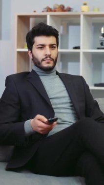 Takım elbiseli şık bir adam, akıllı telefonuna dalmış, koltukta dinleniyor. Balıkçı yakalı başka bir adam uzaktan kumandalı bir düğmeye basar ve rahat bir atmosfer yaratır.