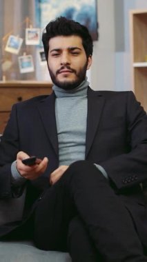 Bu videoda, takım elbiseli bir adam çeşitli ortamlarda teknolojiyle etkileşime geçiyor, uzaktan kumanda ve medya aygıtları konusunda yeteneğini gösteriyor.