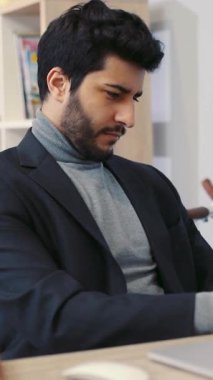 Şık bir takım elbise ve balıkçı yaka giyen sofistike bir adam modern bir masada dizüstü bilgisayarla oturuyor ve çalışırken profesyonellik ve güven yayıyor.