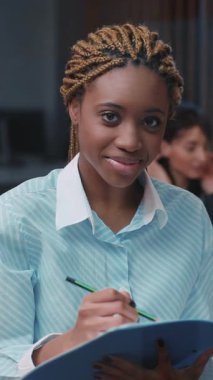 Modern ofis ortamında özverili ve odaklanmış genç bir kadın özenle önemli notlar yazıyor.