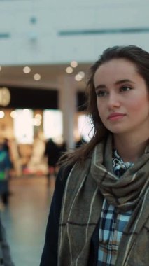 Şık bir atkı ve ekose gömlek giymiş genç bir kadın hareketli ve hareketli bir alışveriş ortamında.