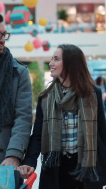 Zarif bir çift, her tarafı renkli süslemelerle dolu canlı bir alışveriş merkezinde birlikte alışveriş yapmaktan hoşlanır.