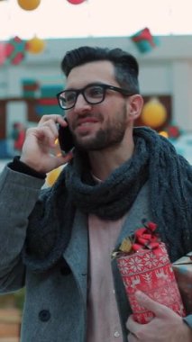 Neşeli bir adam telefonda neşeli bir atmosfer izler, elinde güzel bir hediye taşır.