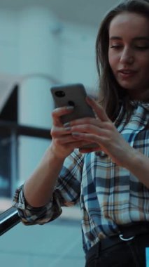 Odaklanmış genç bir kadın, etrafındaki sakin ve rahat bir ortamda akıllı telefonuyla etkileşime geçiyor.