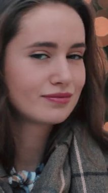 Genç bir kadın, canlı ve renkli ışıklarla çevrili sıcak ve davetkar bir gülümseme ile düşünceli bir şekilde bakıyor.