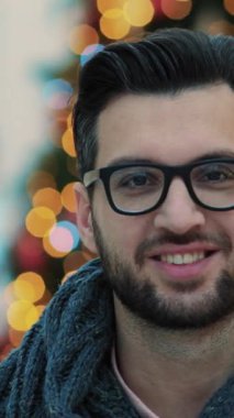 Gözlüklü düşünceli genç bir adam arka planda bulanık renkli ışıklarla yan tarafa bakıyor..