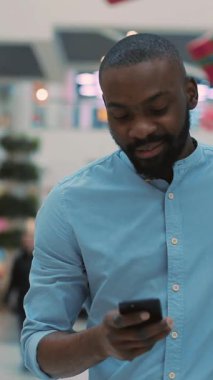 Mavi gömlekli genç bir adam havaalanında dikiliyor, elinde akıllı bir telefonla yukarı bakıyor.