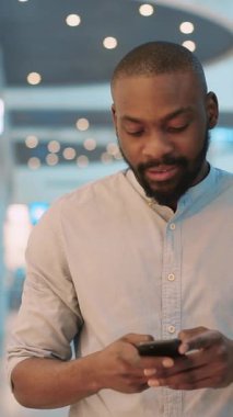 Şık ve şık bir adam, modern çağdaş bir çevreye dalmış akıllı telefonuna dikkatle odaklanır.