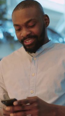 Odaklanmış genç bir adam, canlı çağdaş bir ortamda konumlanırken akıllı telefonuyla derinden ilgilenir.