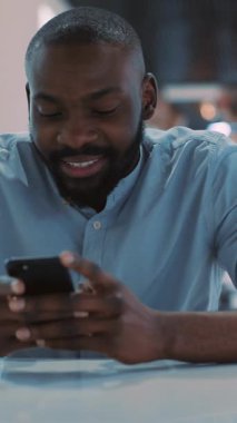 Bugün parlak ve çağdaş bir ofis ortamında akıllı telefon kullanan odaklanmış bir adam gülümsüyor.