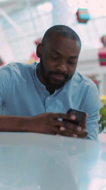 Mavi gömlekli bir adam dikkatle akıllı telefonuna odaklanıyor ve modern iletişimin özünü gözler önüne seriyor.