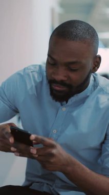 Modern bir ofis ortamında, genç bir adam dikkatle akıllı telefonuna odaklanır.