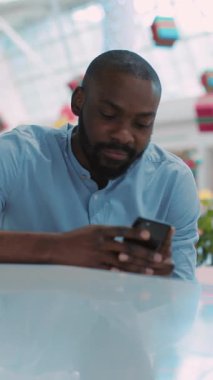 Bir adam modern, çağdaş ofis ortamında bir masada otururken dikkatle akıllı telefonuna odaklanır.