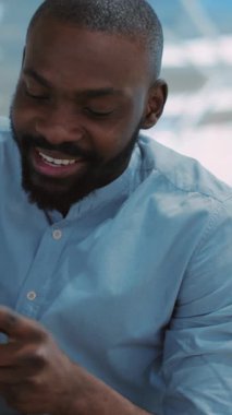 Neşeli bir adam, modern ofis ortamında mutluluğunu ifade eden akıllı telefonuyla neşe içinde etkileşim içindedir.