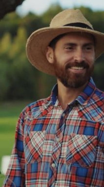 Kareli gömlek giymiş neşeli bir çiftçi, yemyeşil, canlı bir tarlanın ortasında dikilirken neşeyle gülümsüyor.